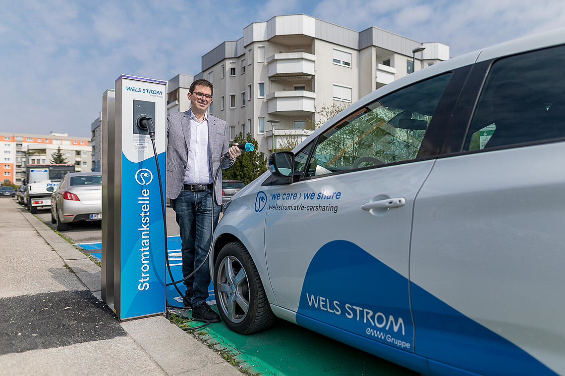 Herr Vollmann an einer Ladestation und neben einem Elektroauto vom eww E-Carsharing